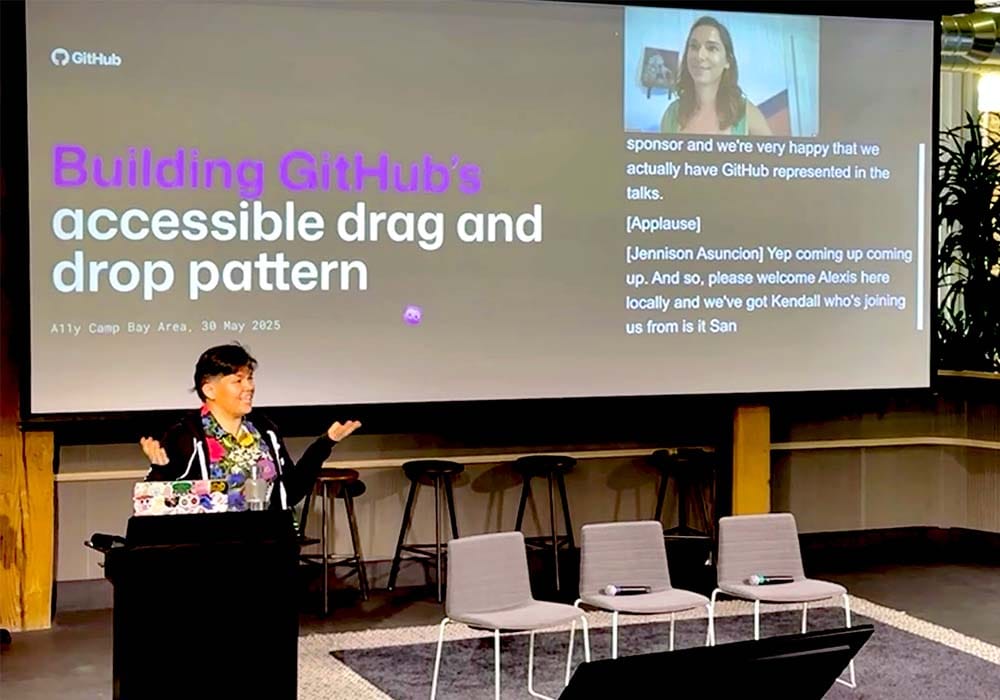 A smiling Alexis, wearing a colorful button-down shirt and GitHub hoodie, gestures with both palms up while Kendall observes from her virtual vantage point. On the screen behind Alexis is the title slide to their talk with the headline: Building GitHub’s accessibility drag and drop pattern.